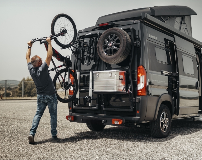 Homme qui pose un vae sur un porte vélo d'un fourgon aménagé 